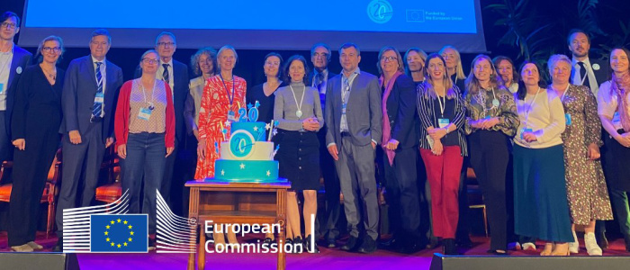 A group of attendees of the Erasmus Mundus 20th Anniversary conference on stage with a 20th anniversary cake