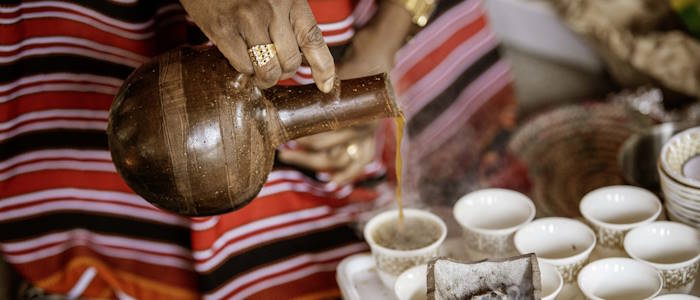 A woman pouring coffee from an earthenware jug into china cups