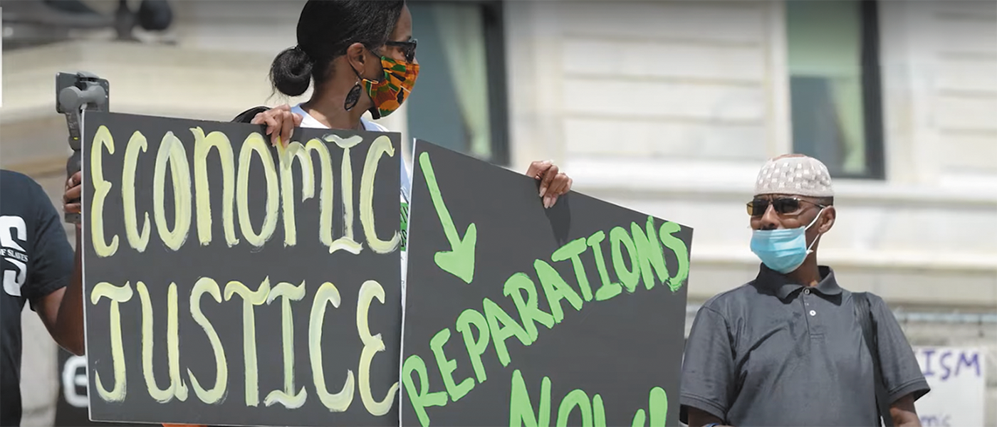 Protester with placards calling for economic justice and reparations