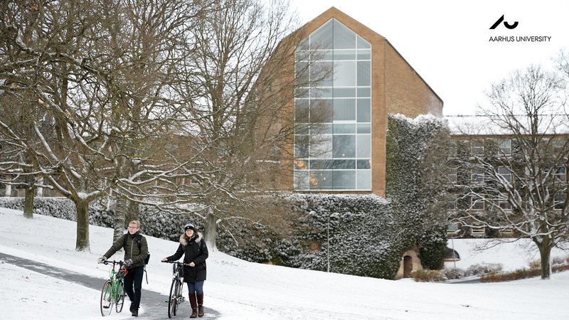 Aarhus University in winter. Snow on the ground with two people in front of a building