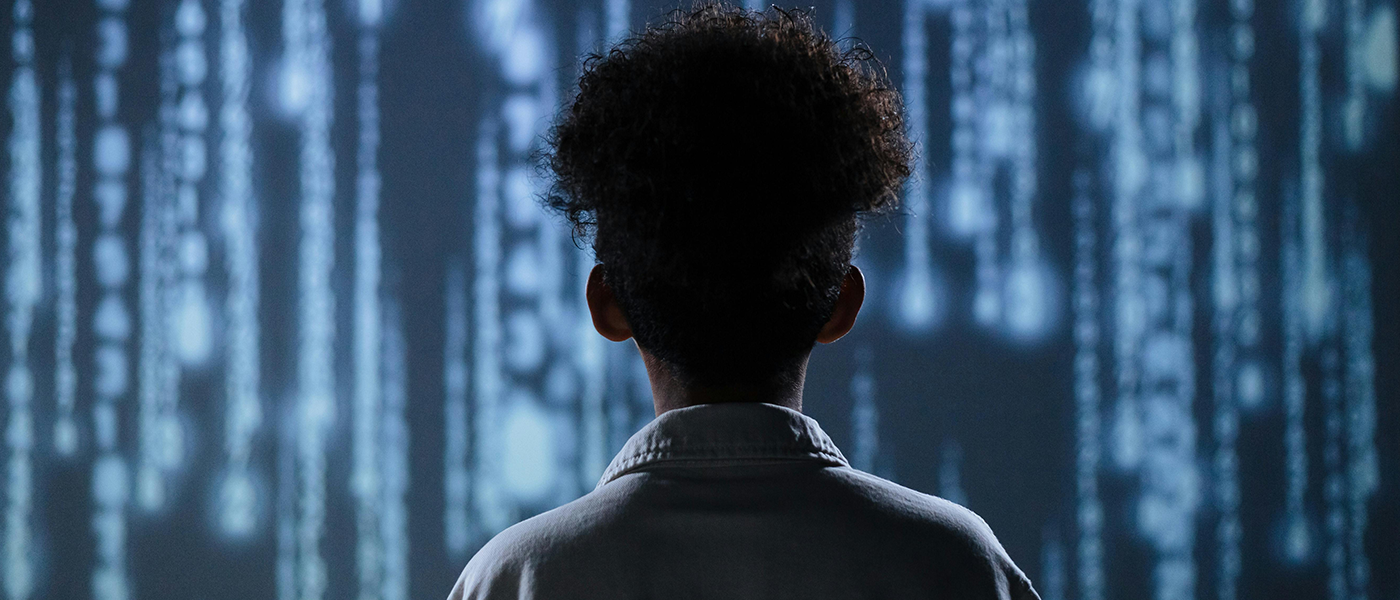 A young person standing in front of a screen showing data streams
