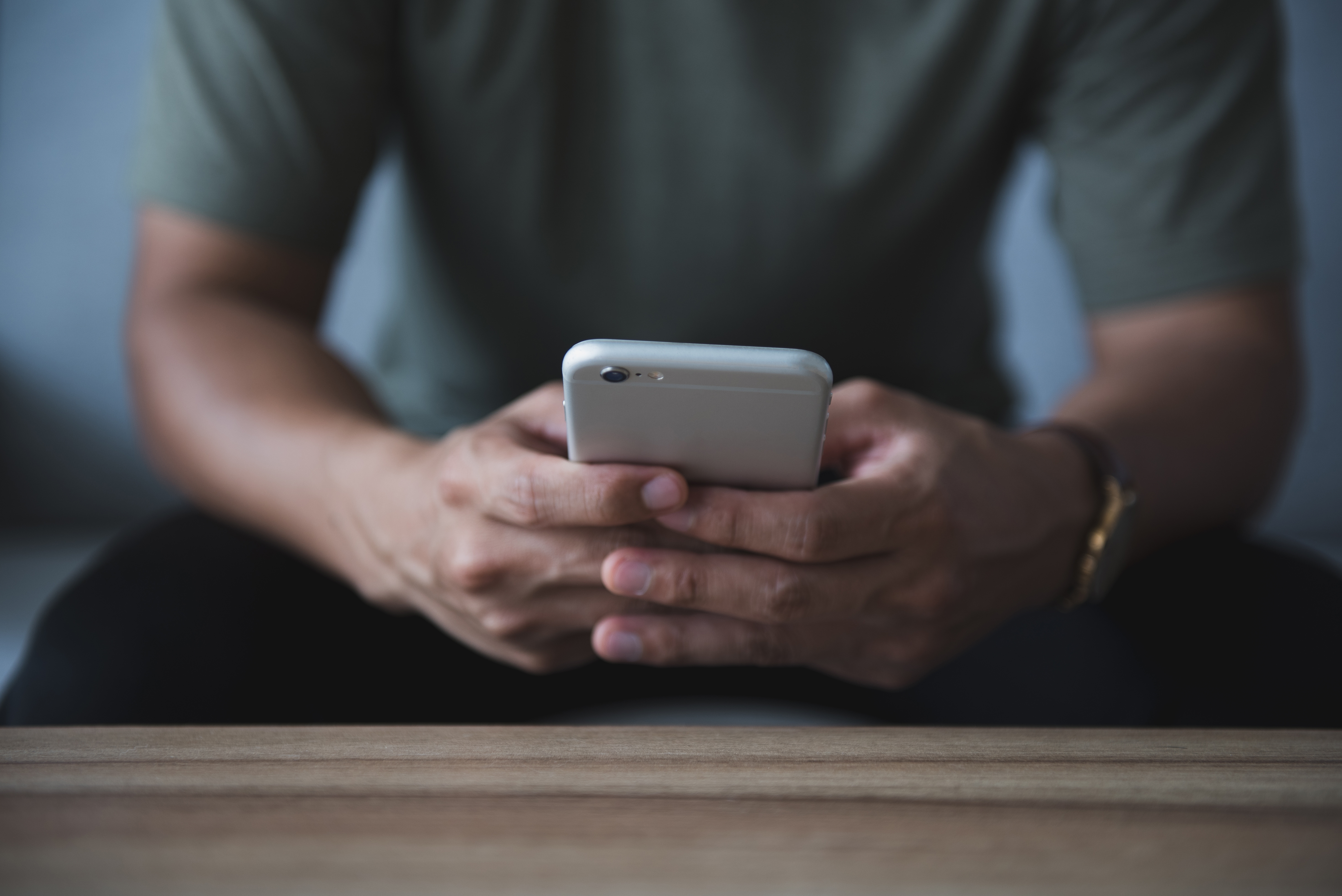Young man hand holding cell phone on the sofa in the living room. He was reading and answering emails and shopping online on weekends at home.