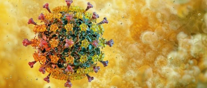 Close-up illustration of a coronavirus particle with a spherical shape, covered in spike proteins. The virus appears in shades of yellow, orange, and red, set against a blurred golden background.