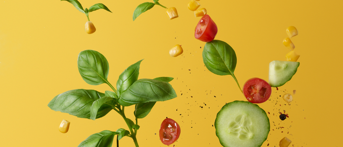 Cucumber, tomatoes and avocados captured mid-air on bold yellow background