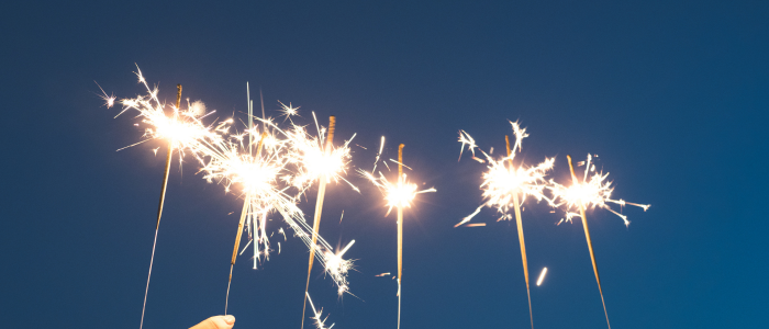 A row of sparklers being held upright against a dark blue night sky