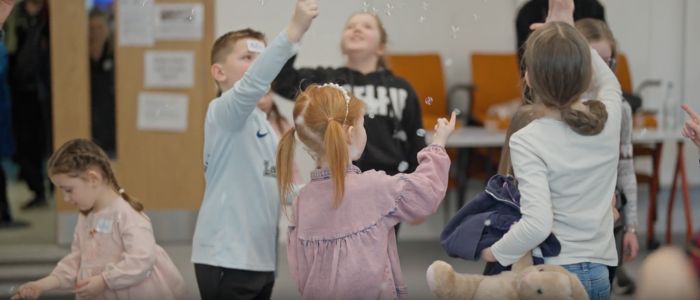 Children playing together indoors, reaching up toward floating bubbles.