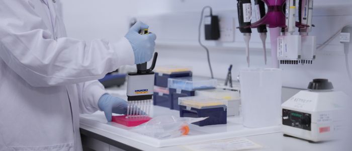 Scientist using a multichannel pipette at a lab bench with equipment and samples.