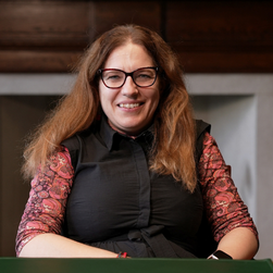 A headshot of a smiling woman wearing glasses with long brown hair