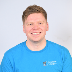 A headshot of a smiling man wearing cobalt blue UofG t-shirt, with short ginger hair