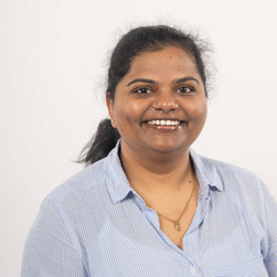 A headshot of a smiling South Asian woman with her hair in a pony tail wearing a striped white and blue shirt