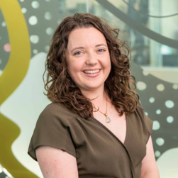 A headshot of a smiling woman with long, curly brown hair