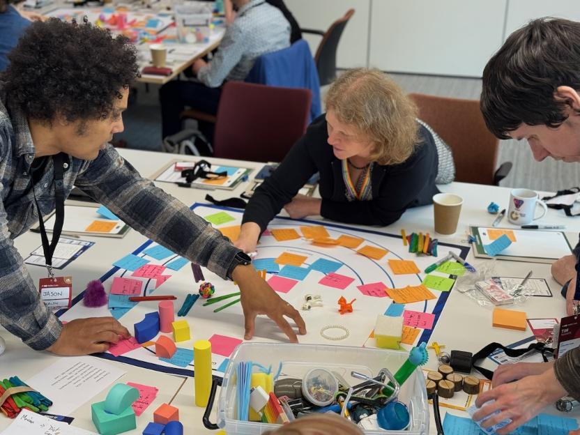 Two people leaning over a table covered with post-it notes and random items