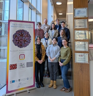 6 women and 4 men stood posing on a staircase next to a floor-to-ceiling window. A promotional SCMI pop-up banner is in the foreground.