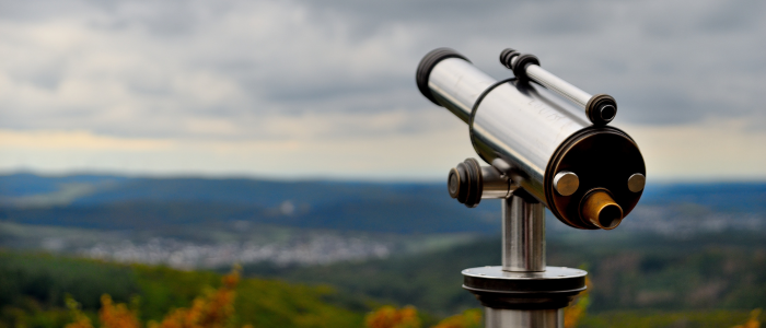 A telescope pointing to sky with landscape in background.
