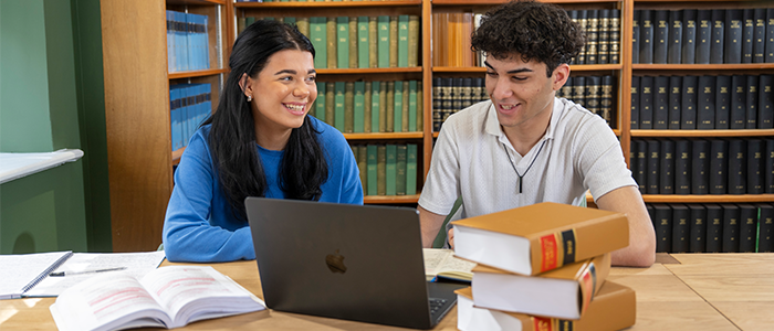 One female and one male student smiling at laptop with books