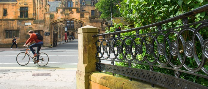 A student on a bike cycles past University Gardens and the main entrance