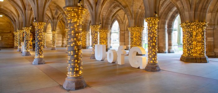 Large ornamental UofG letters on display in the Cloisters, with fairy lights around the pillars