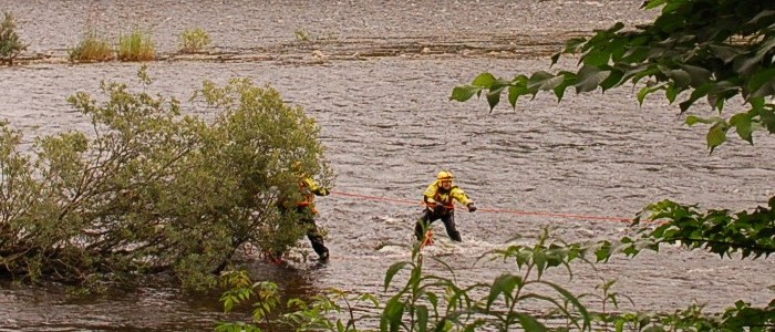 Two men in fast moving water pulling on rope
