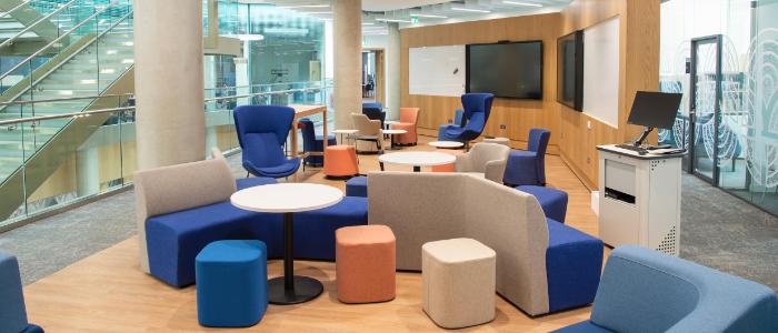 Collaborative working area featuring 5 small round tables, soft seating, white boards, and a screen, overlooking the ARC atrium